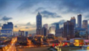 Blurry cityscape with illuminated buildings at dusk.