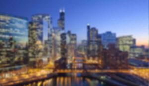 Blurry cityscape with illuminated skyscrapers at dusk.