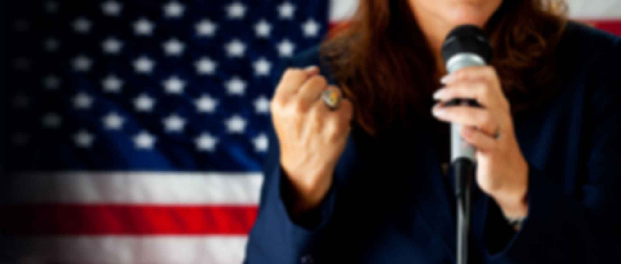 Person speaking with American flag backdrop.