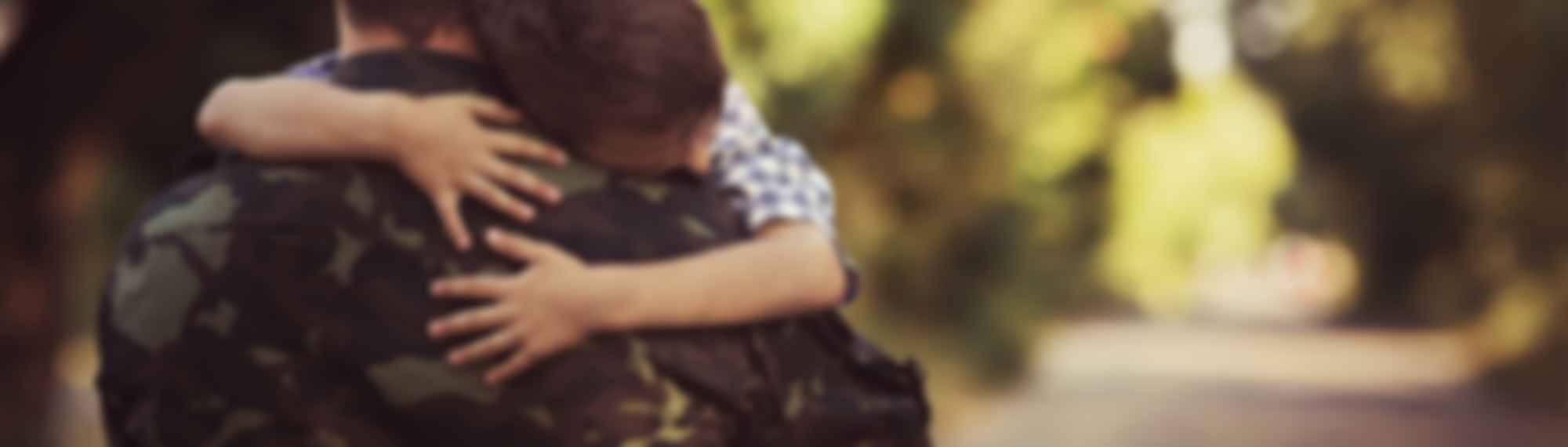 Child hugging person in camouflage uniform.