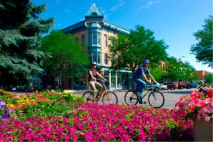Cyclists passing colorful flowers and historic building.