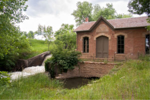 Brick building beside small waterfall and greenery.