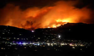 Wildfire illuminating night sky over cityscape.